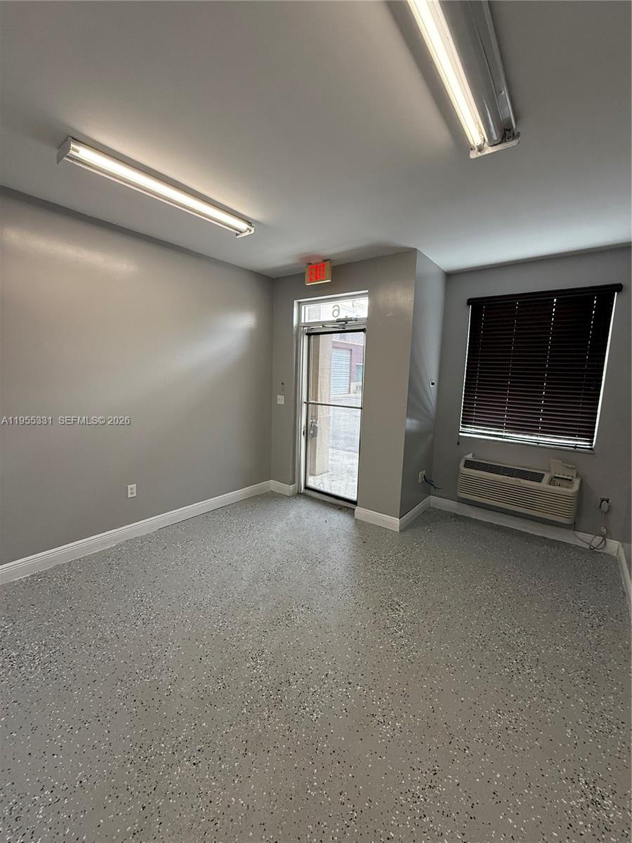 An empty room features gray walls, a speckled epoxy floor, fluorescent lighting, and an air conditioner — 15075 SW 137th St # 6, Miami FL 33196, MIAMI, FL