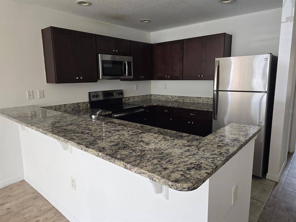A kitchen features dark wood cabinets, granite countertops, and stainless steel appliances — 168 BOWIE LANE UNIT 101, KISSIMMEE, FL