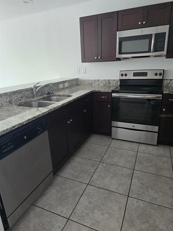 A kitchen features dark wood cabinets, stainless steel appliances, and granite countertops over tiled floors — 168 BOWIE LANE UNIT 101, KISSIMMEE, FL