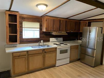 A kitchen features wood-paneled walls, wooden cabinets, a stainless steel refrigerator, and light-colored countertops — 7032 SE 170TH AVENUE ROAD, OCKLAWAHA, FL