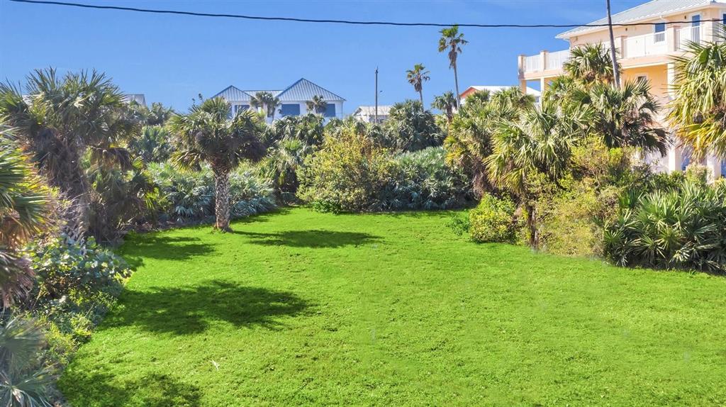 A grassy vacant lot is surrounded by palm trees and nearby residential buildings — 0 S ATLANTIC AVE, NEW SMYRNA BEACH, FL