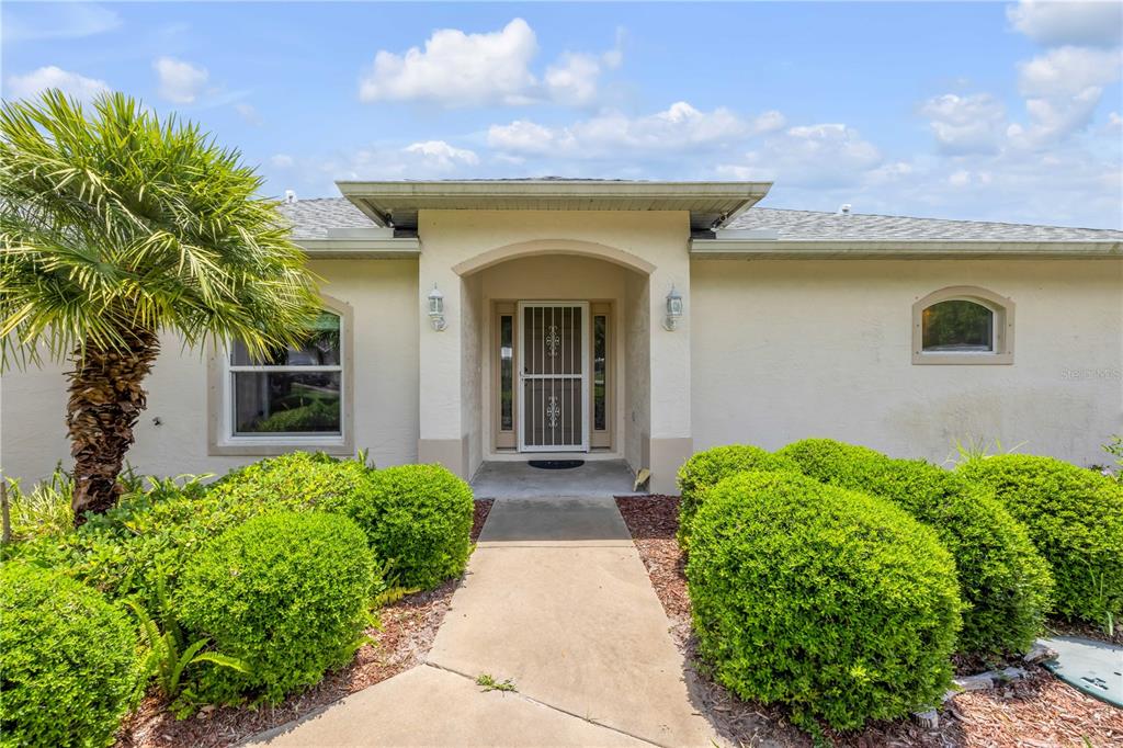 A beige house exterior features a front walkway leading to a covered entryway with landscaping — 192 AZALEA ROAD, EDGEWATER, FL