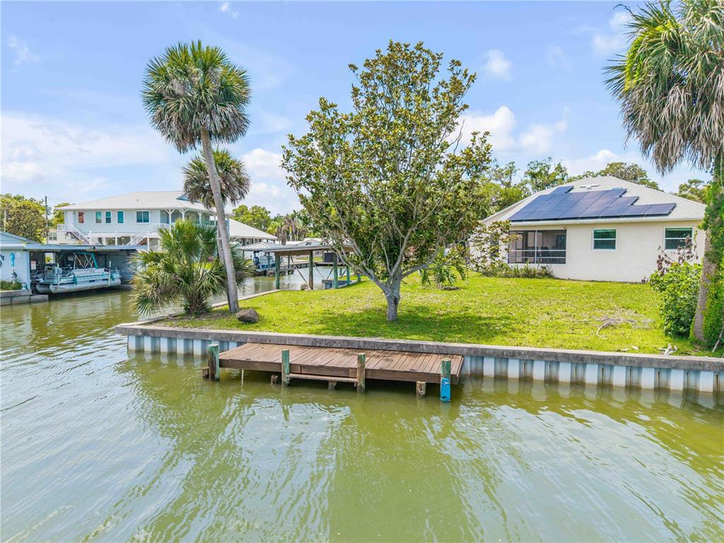A waterfront house with solar panels, a wooden dock, and palm trees on a canal — 192 AZALEA ROAD, EDGEWATER, FL