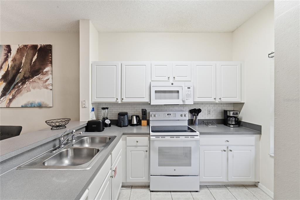 A kitchen features white cabinets, gray countertops, a white stove, and a subway tile backsplash — 2743 SUN KEY PLACE, KISSIMMEE, FL