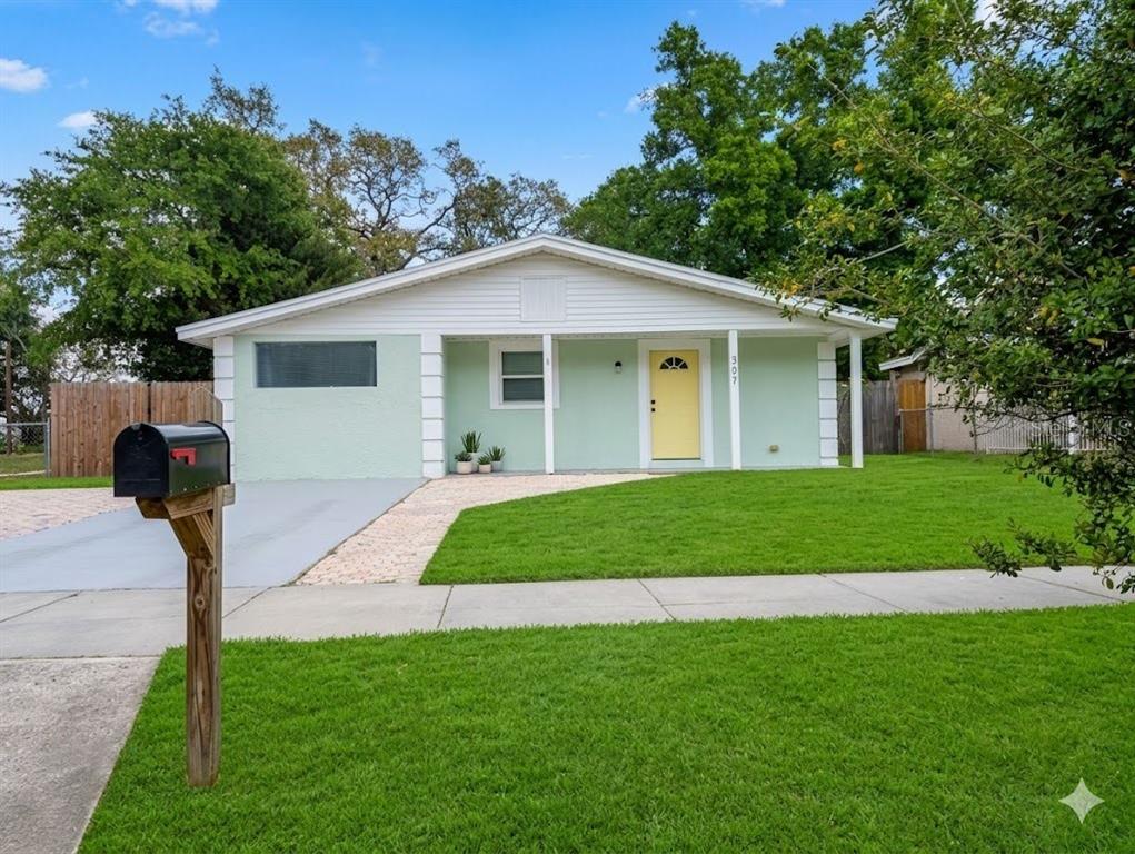 A light green single-story house features a yellow front door and a paved driveway — 307 W WOODLAWN AVENUE, TAMPA, FL
