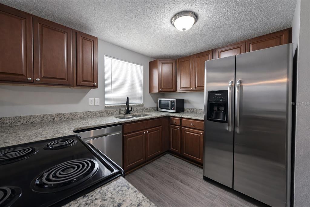 A kitchen featuring dark wood cabinets, granite countertops, stainless steel appliances, and wood-look flooring — 307 W WOODLAWN AVENUE, TAMPA, FL