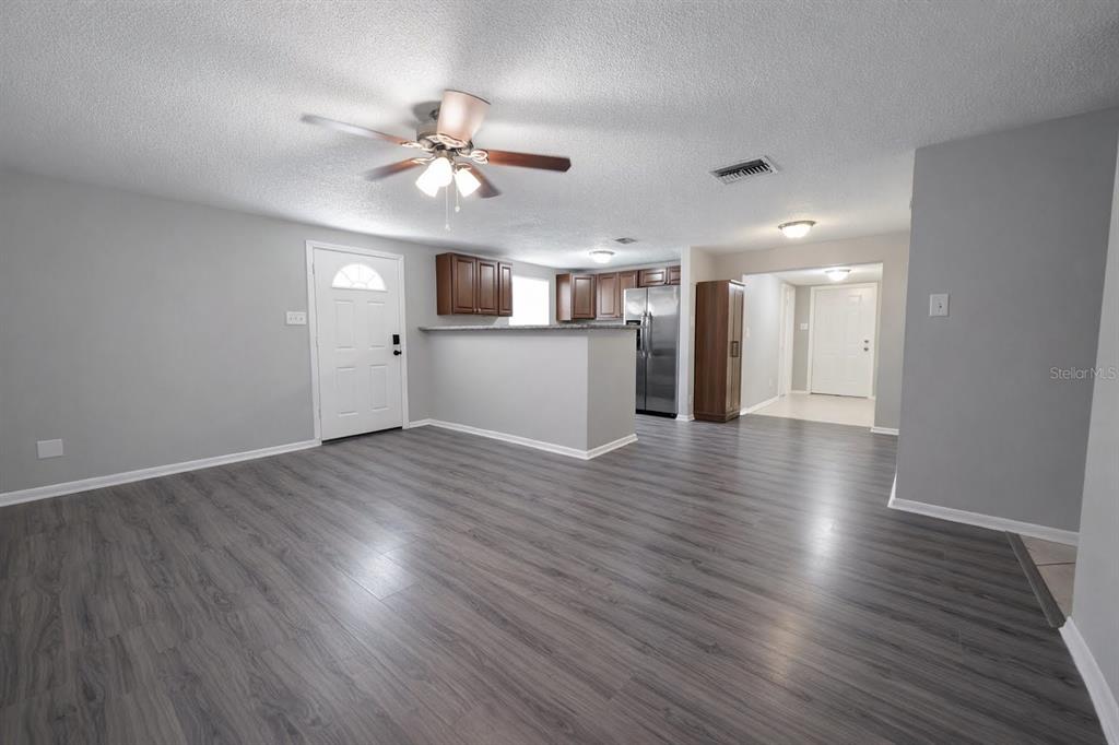 A living room with gray walls and wood-look flooring opens to a kitchen with cabinets — 307 W WOODLAWN AVENUE, TAMPA, FL
