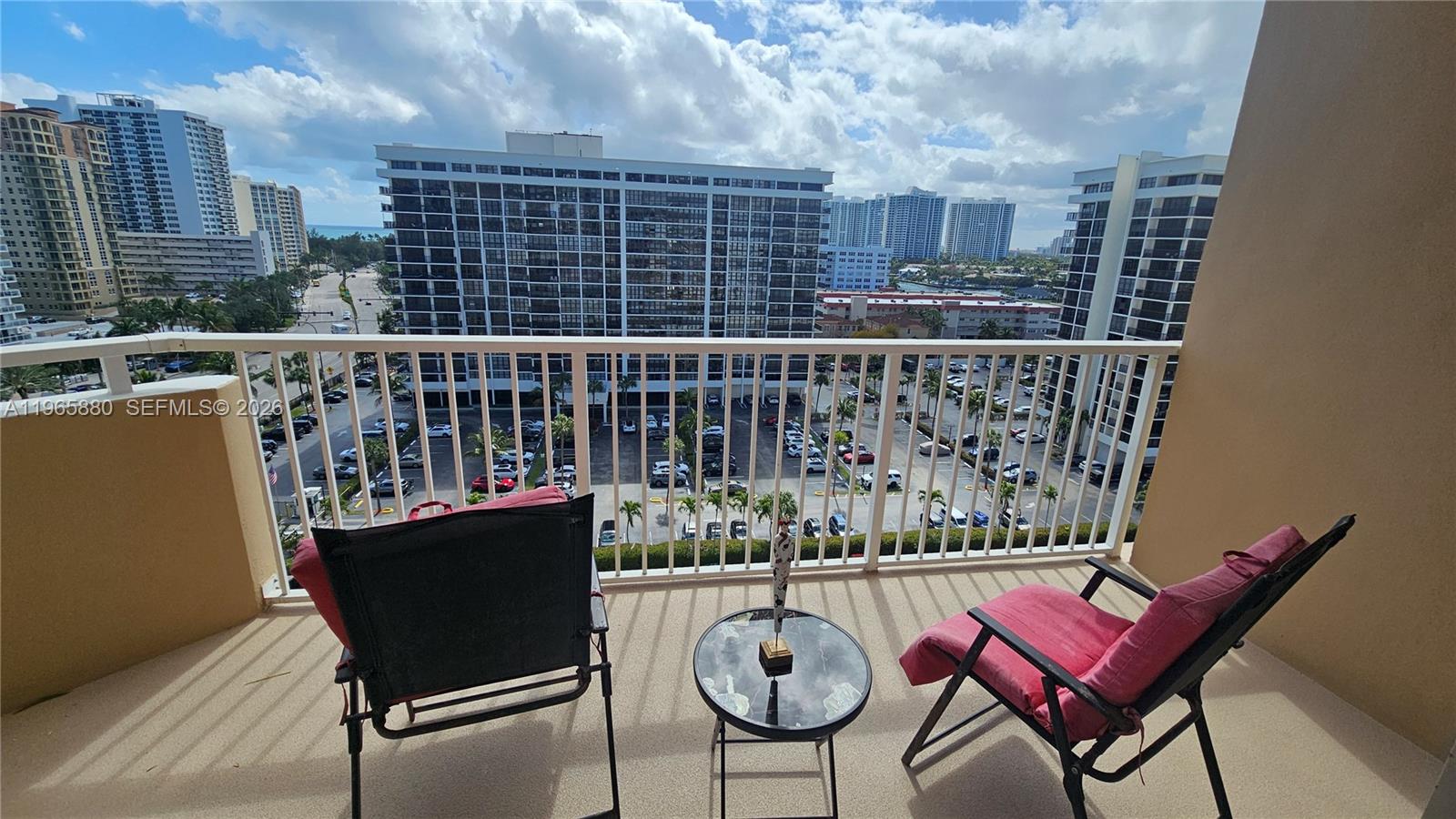 A balcony with two chairs and a small table overlooks a parking lot and buildings — 1985 S Ocean Dr # 10J, Hallandale Beach FL 33009, HALLANDALE BEACH, FL