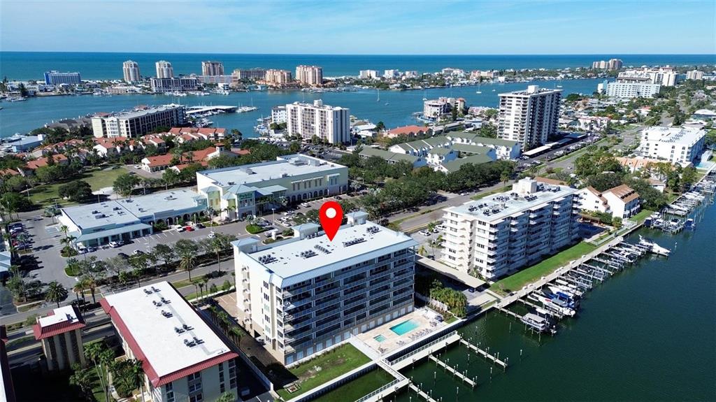 An aerial view shows a multi-story waterfront condominium building with a pool and boat slips — 125 ISLAND WAY UNIT 403, CLEARWATER, FL