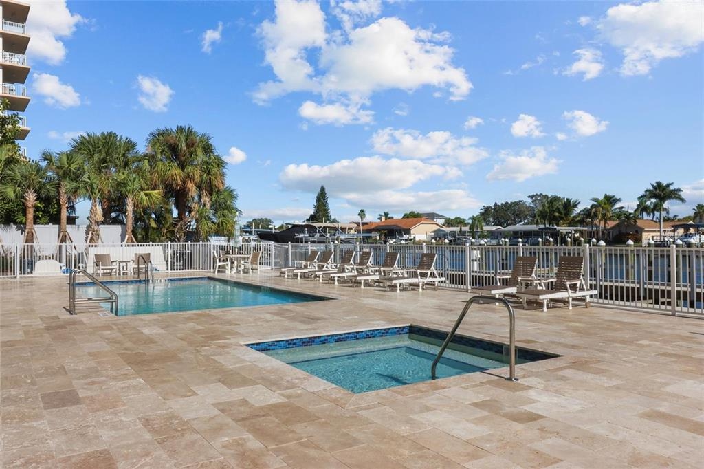 A swimming pool and hot tub on a tiled patio overlooking a canal with boats — 125 ISLAND WAY UNIT 403, CLEARWATER, FL