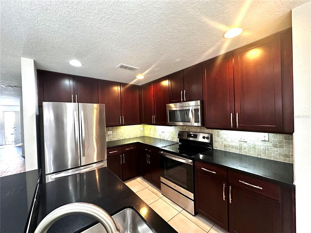 A kitchen features dark wood cabinets, black countertops, stainless steel appliances, and a tiled backsplash — 3845 SILVERBELL LOOP, OVIEDO, FL