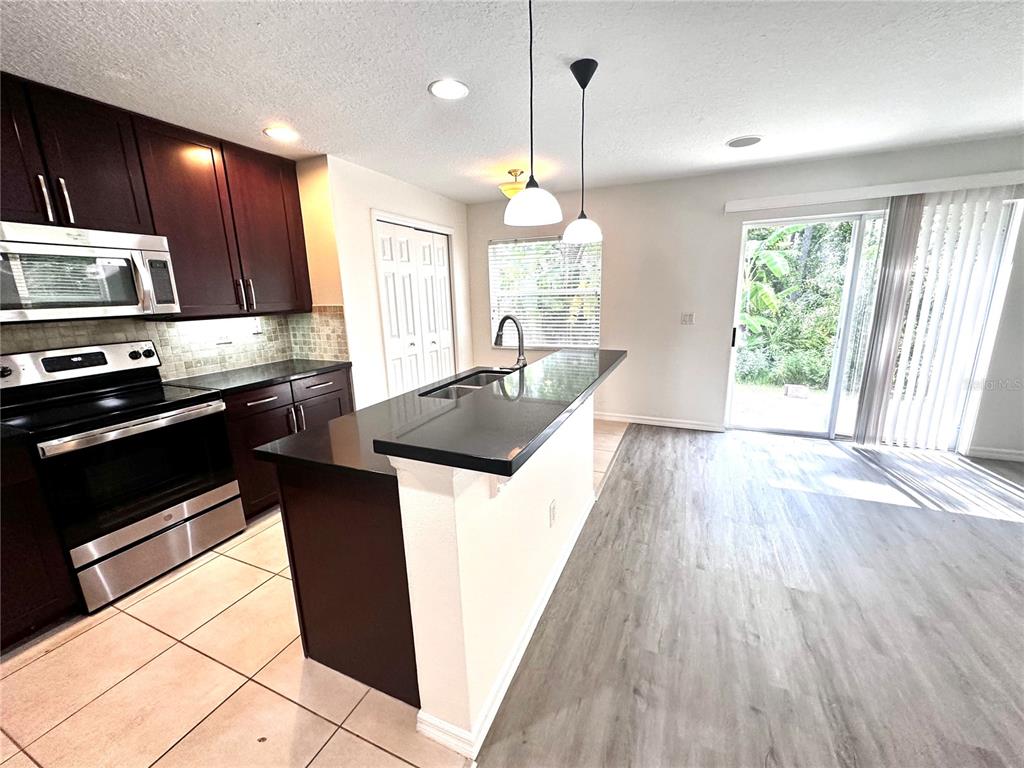 A kitchen features dark wood cabinets, black countertops, stainless steel appliances, and light flooring — 3845 SILVERBELL LOOP, OVIEDO, FL