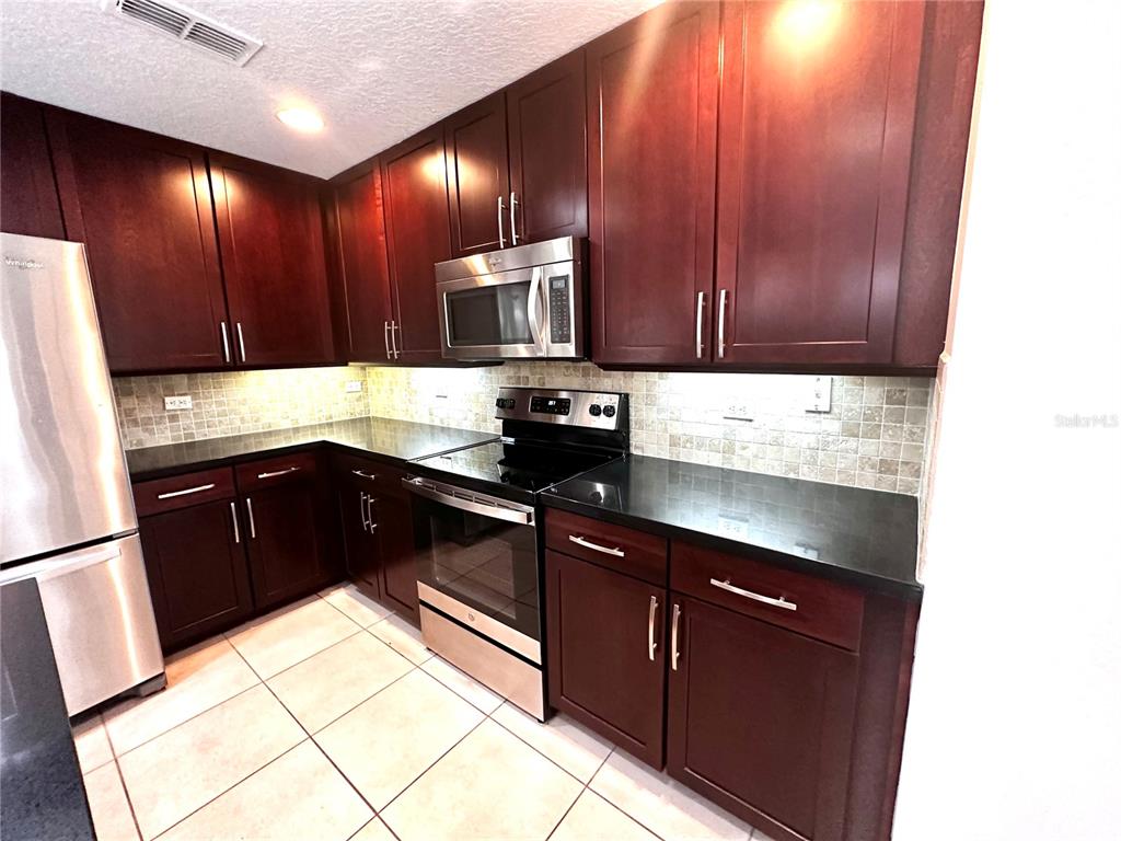 A kitchen features dark wood cabinets, stainless steel appliances, black countertops, and tiled backsplash — 3845 SILVERBELL LOOP, OVIEDO, FL