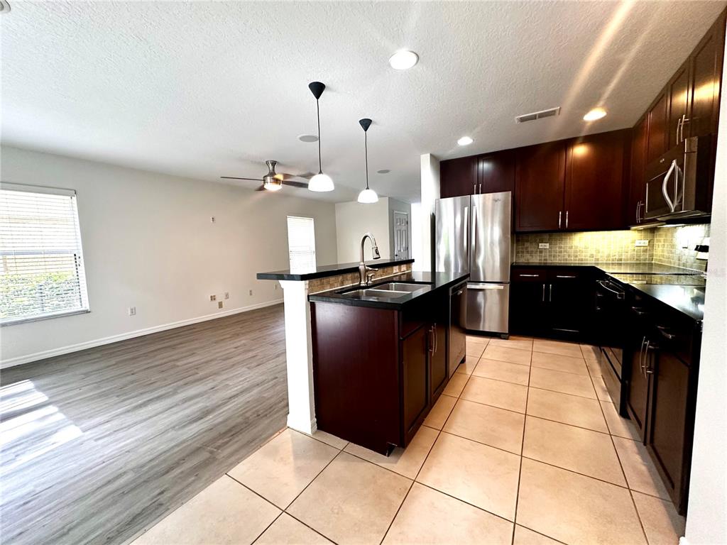 A kitchen with dark wood cabinets and stainless steel appliances overlooks a living area — 3845 SILVERBELL LOOP, OVIEDO, FL