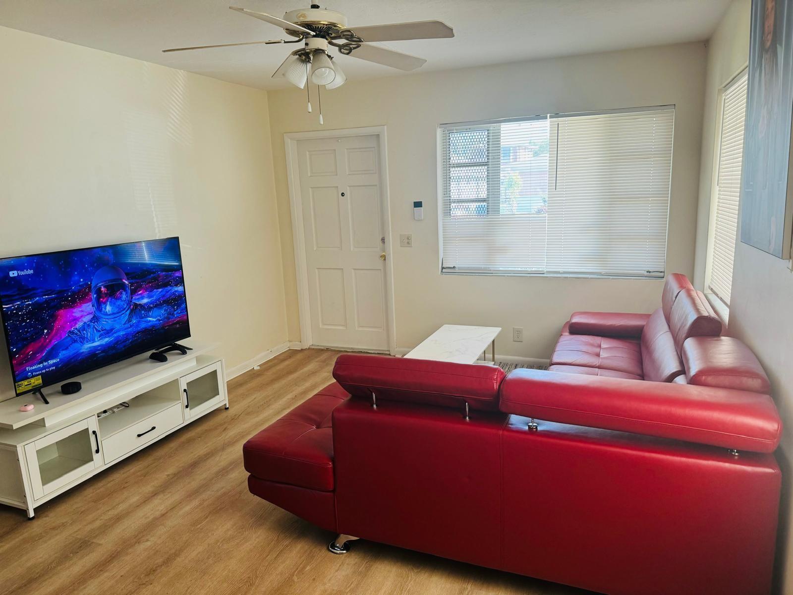 A living room features a red sectional sofa, a white media console, and light wood flooring — 958 W 4th Street, Riviera Beach FL 33404, RIVIERA BEACH, FL