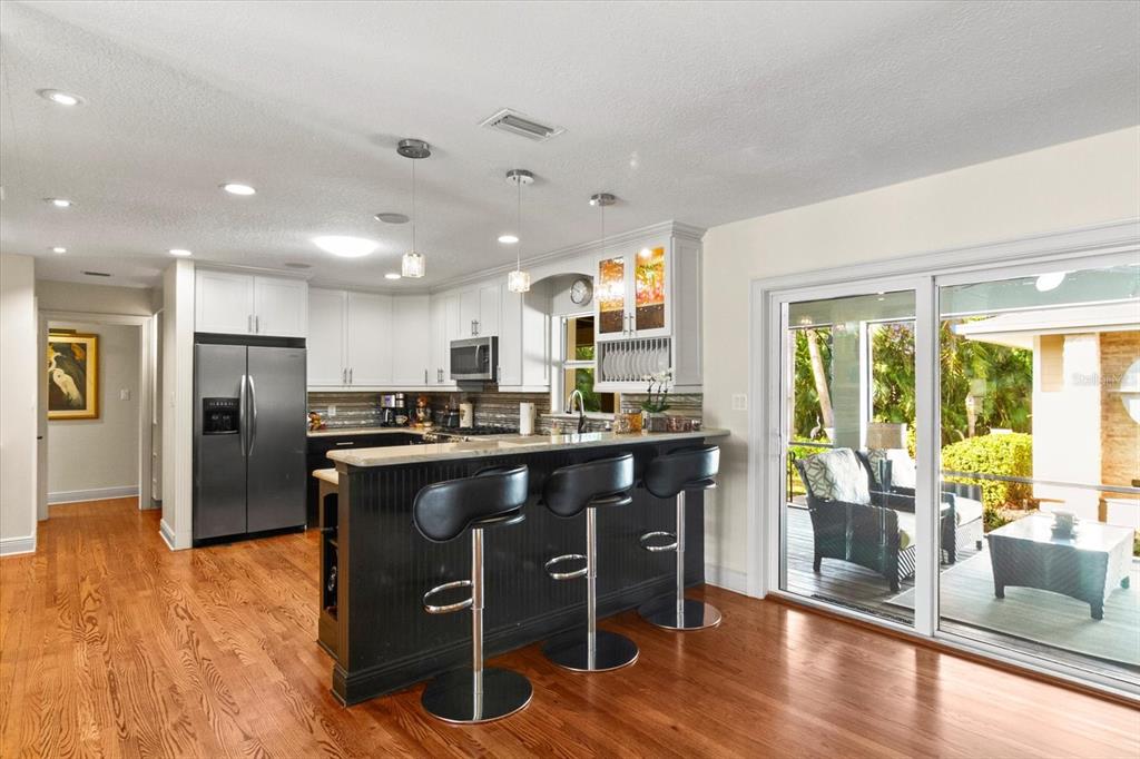 A kitchen features white upper cabinets, a black island with bar stools, and sliding glass doors — 1538 S ORANGE AVENUE, SARASOTA, FL