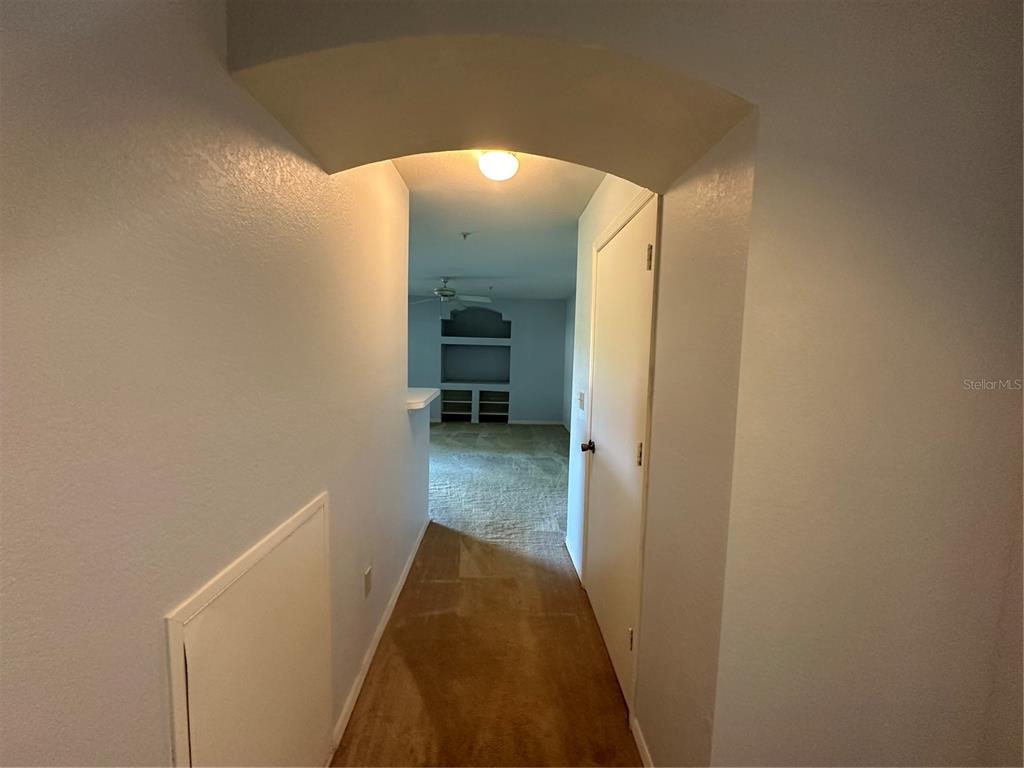 A carpeted hallway leads through an arched doorway into a living area with large windows — 7270 WESTPOINTE BOULEVARD UNIT 916, ORLANDO, FL