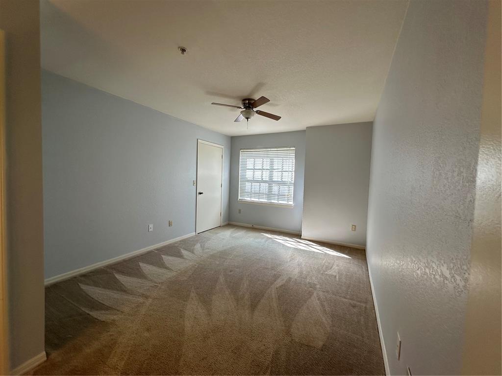 An empty bedroom with light blue walls, beige carpet, a ceiling fan, and a window — 7270 WESTPOINTE BOULEVARD UNIT 916, ORLANDO, FL