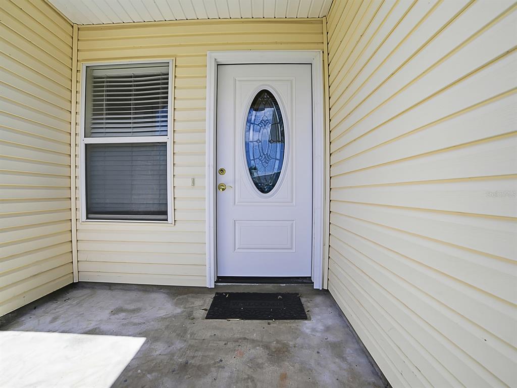 A white front door with an oval glass insert sits on a concrete porch — 32744 WESTWOOD LOOP, LEESBURG, FL