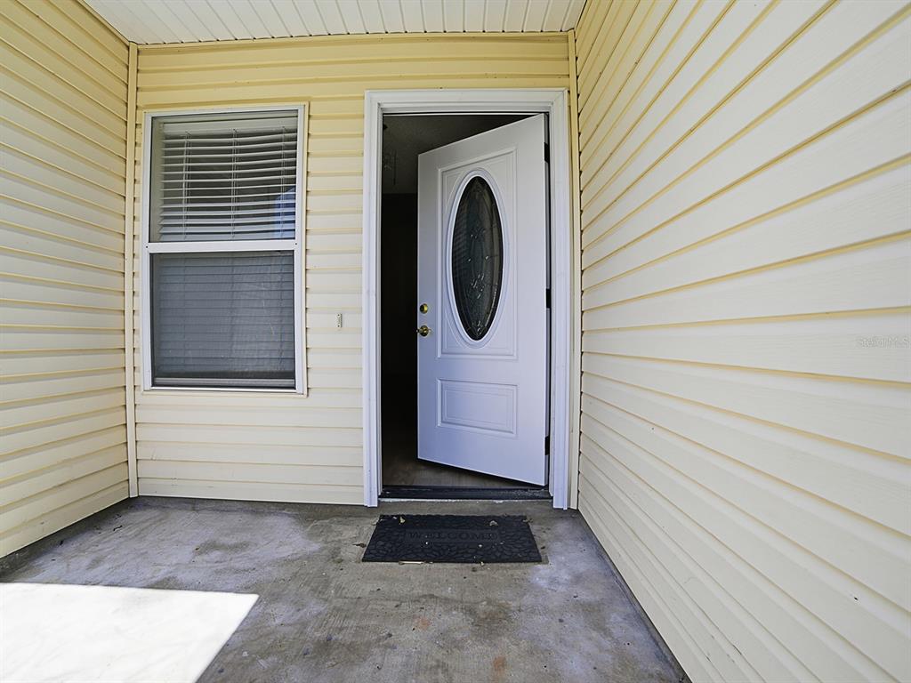 A white front door with an oval glass insert opens onto a concrete porch — 32744 WESTWOOD LOOP, LEESBURG, FL