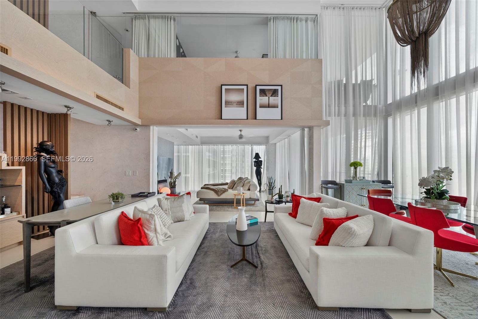 A modern, double-height living room features two white sofas, red accent pillows, and floor-to-ceiling curtains — 1040 Biscayne Blvd # 4607, Miami FL 33132, MIAMI, FL