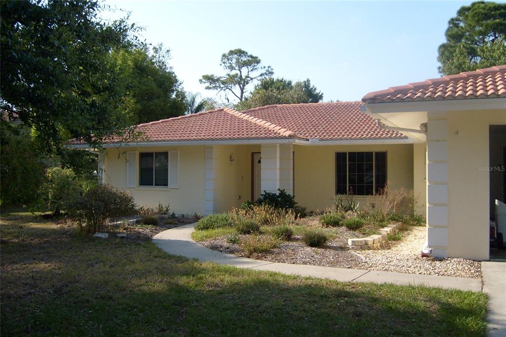 A single-story house with a tiled roof, light-colored stucco walls, and a landscaped front yard — 1876 MID OCEAN CIRCLE, SARASOTA, FL