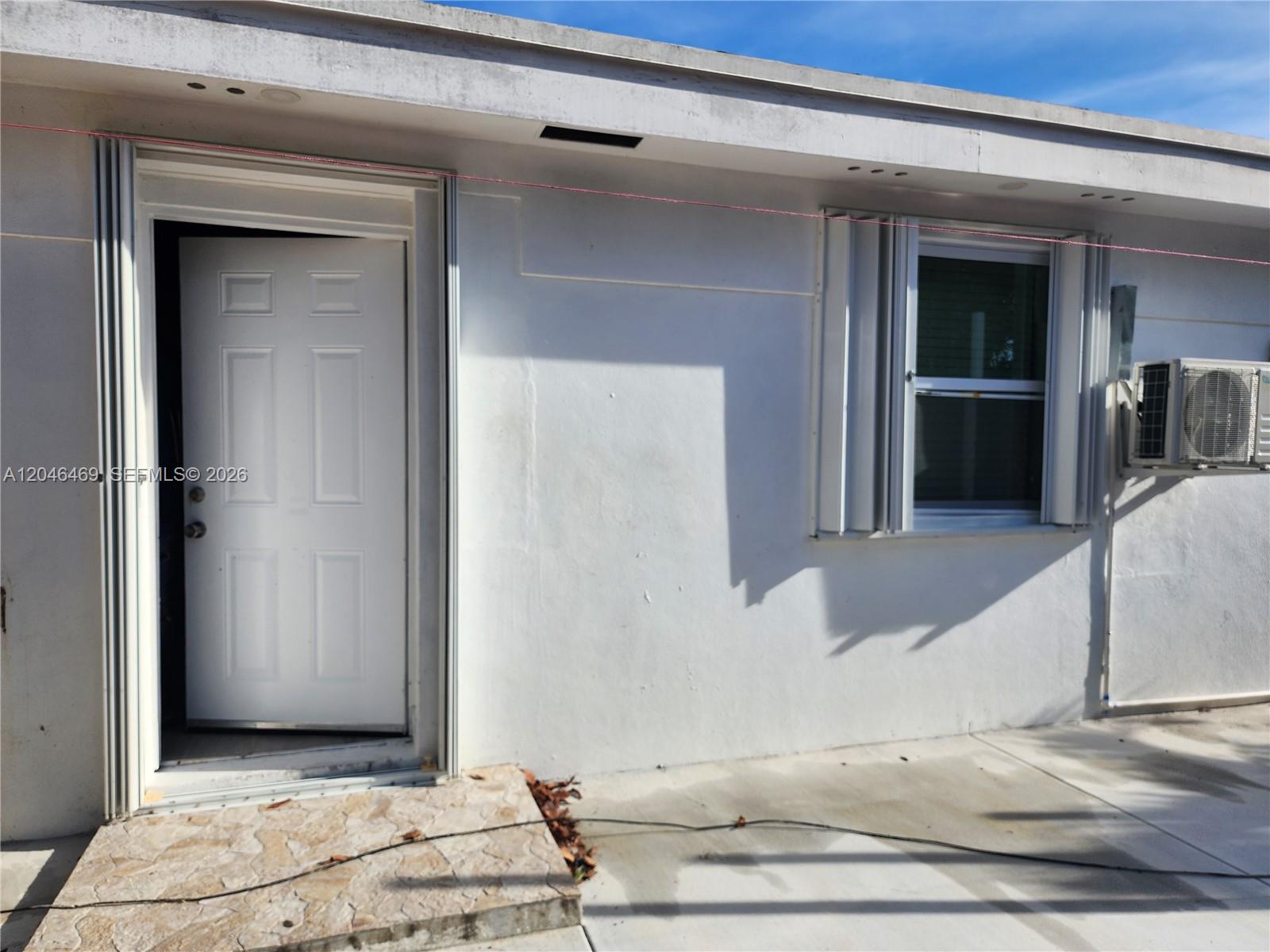 The exterior of a white building features a white door, a window, and an air conditioner — 11461 SW 197th St # A, Miami FL 33157, MIAMI, FL