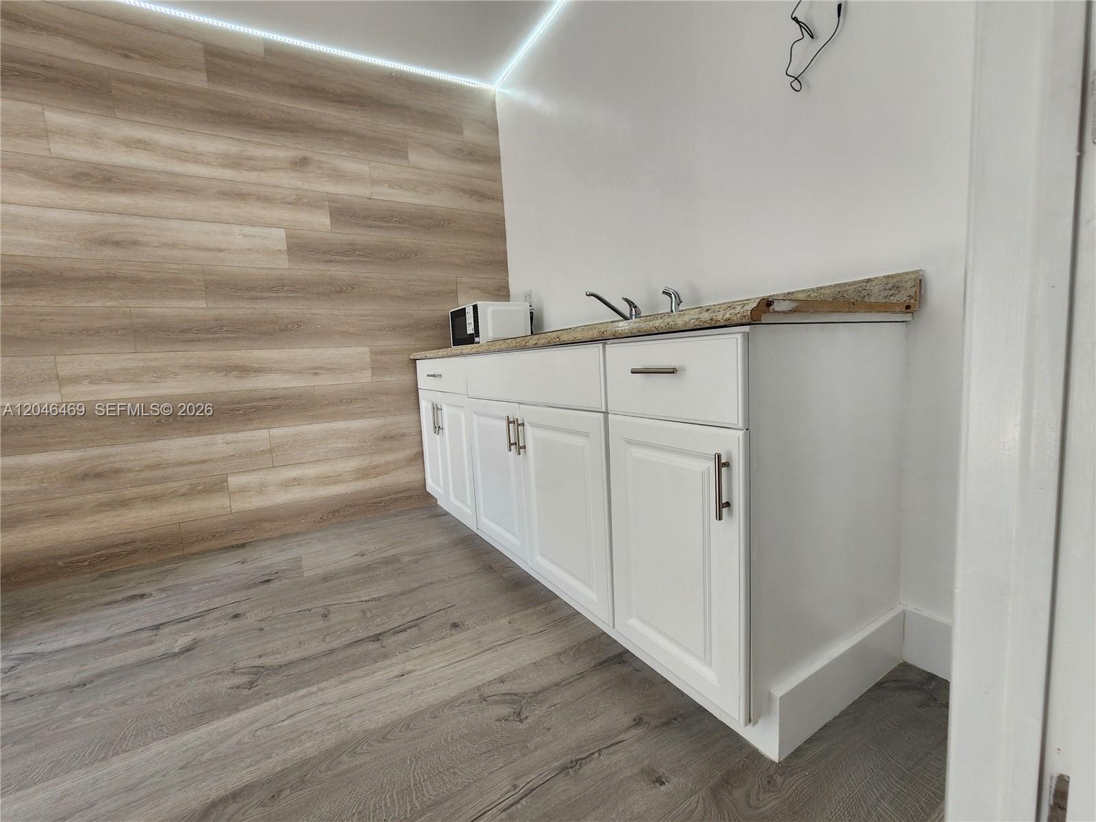 A kitchenette features white cabinets, a granite countertop, and wood-look flooring and wall paneling — 11461 SW 197th St # A, Miami FL 33157, MIAMI, FL