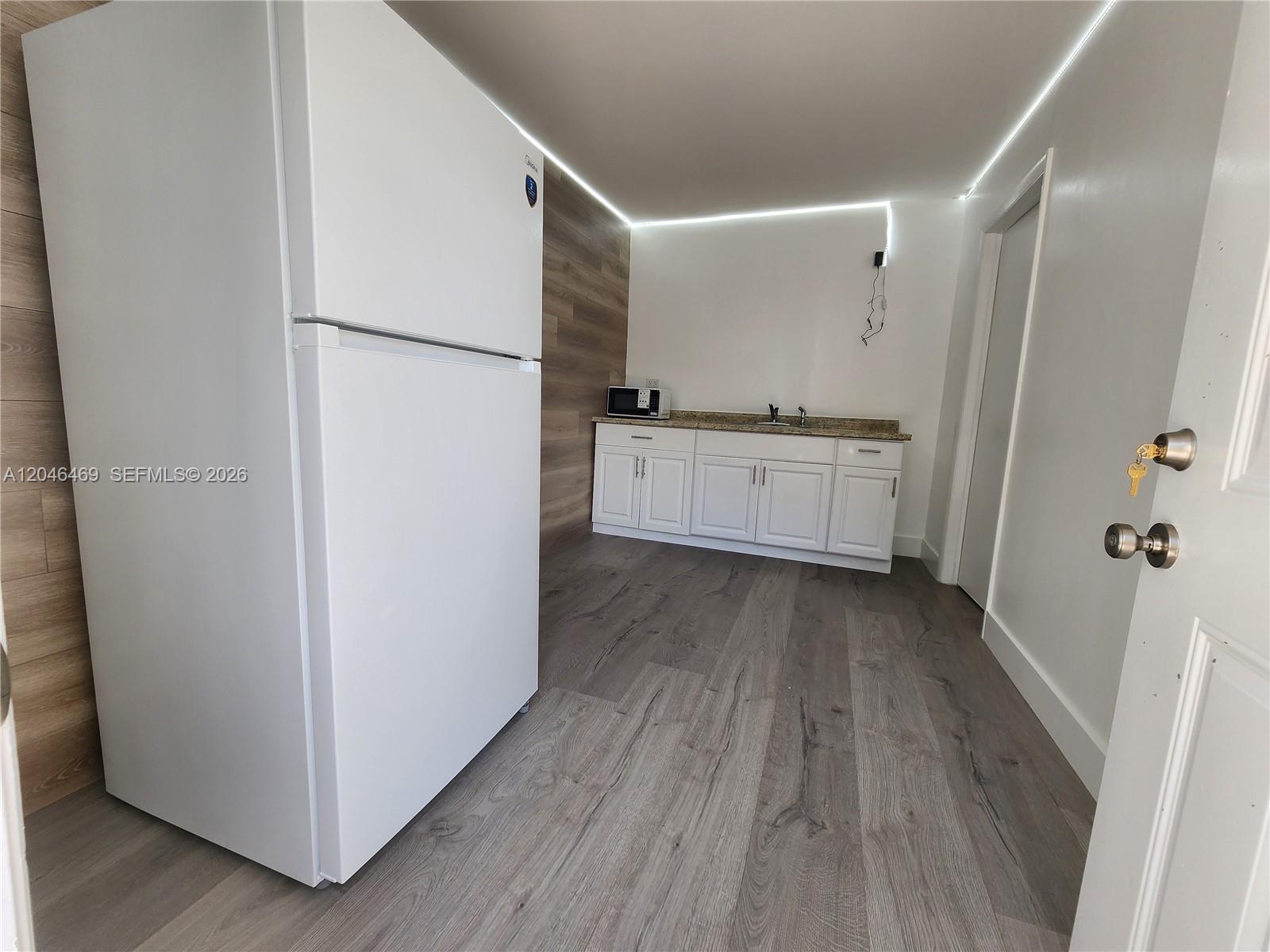 A small kitchen area features white cabinets, a refrigerator, and wood-look flooring — 11461 SW 197th St # A, Miami FL 33157, MIAMI, FL