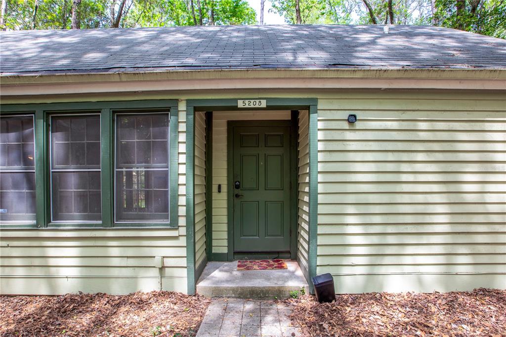 The exterior of a house features light green horizontal siding, a dark green door, and windows — 5208 SW 86TH TERRACE, GAINESVILLE, FL