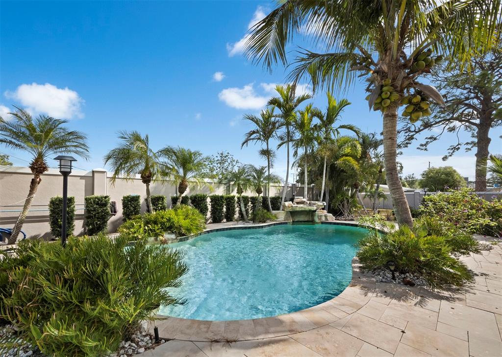 A backyard swimming pool features a rock waterfall, palm trees, and a stone patio — 5618 BRITANNIA DRIVE, SARASOTA, FL