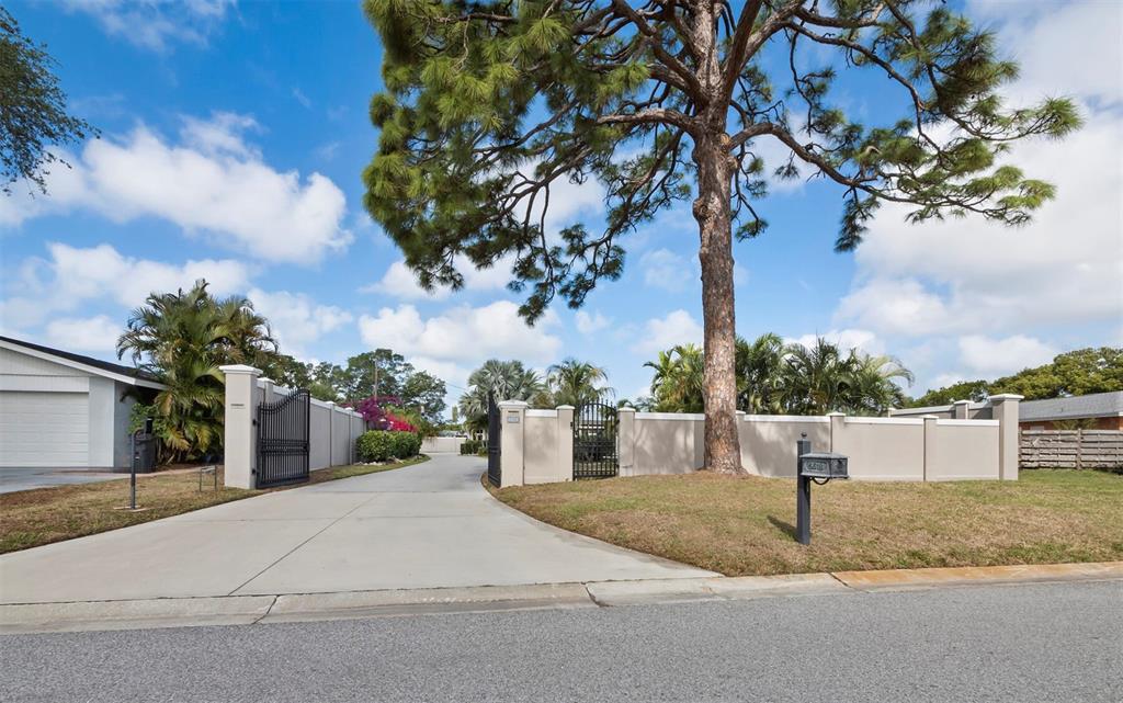 A concrete driveway leads through a gated entrance to a property with a large pine tree — 5618 BRITANNIA DRIVE, SARASOTA, FL