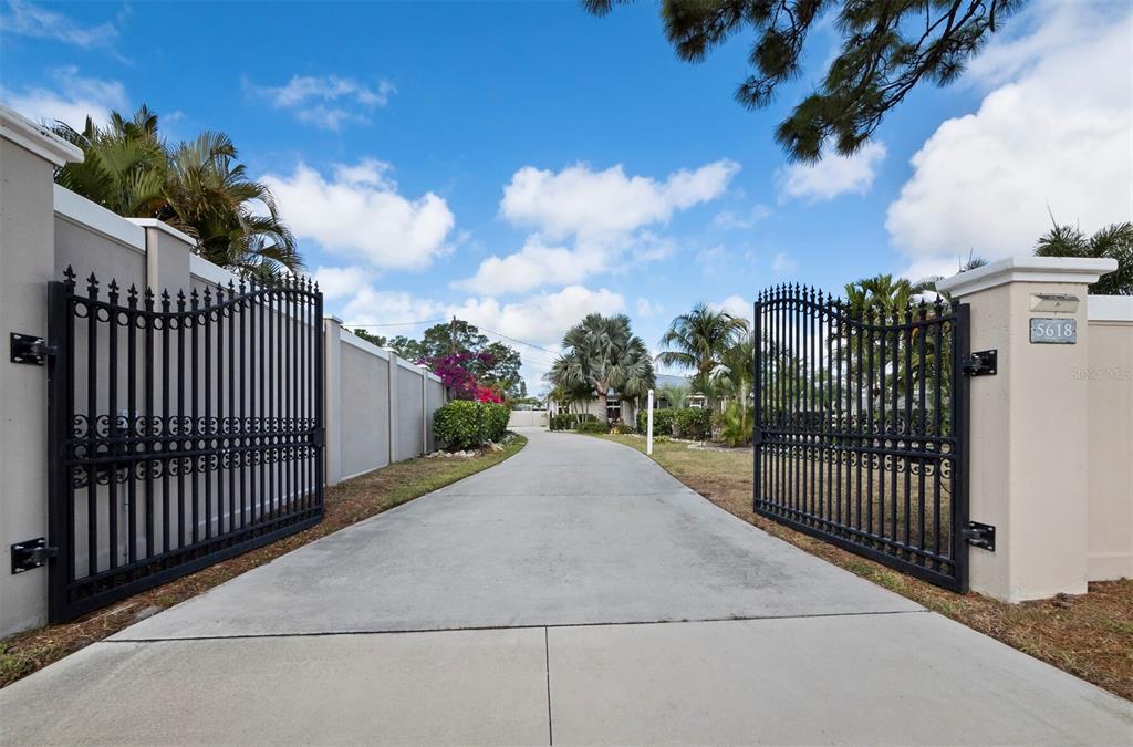 A concrete driveway leads through an open black metal gate toward a residential property — 5618 BRITANNIA DRIVE, SARASOTA, FL