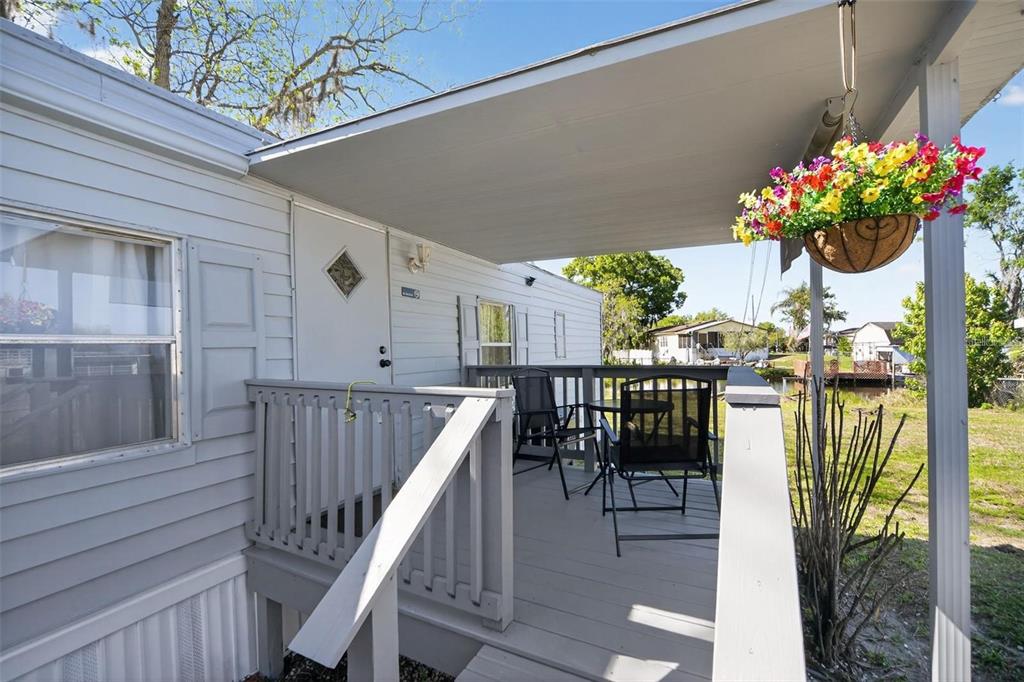 A covered wooden porch with outdoor seating and a hanging flower basket on a mobile home — 2944 PALM CIRCLE, HAINES CITY, FL