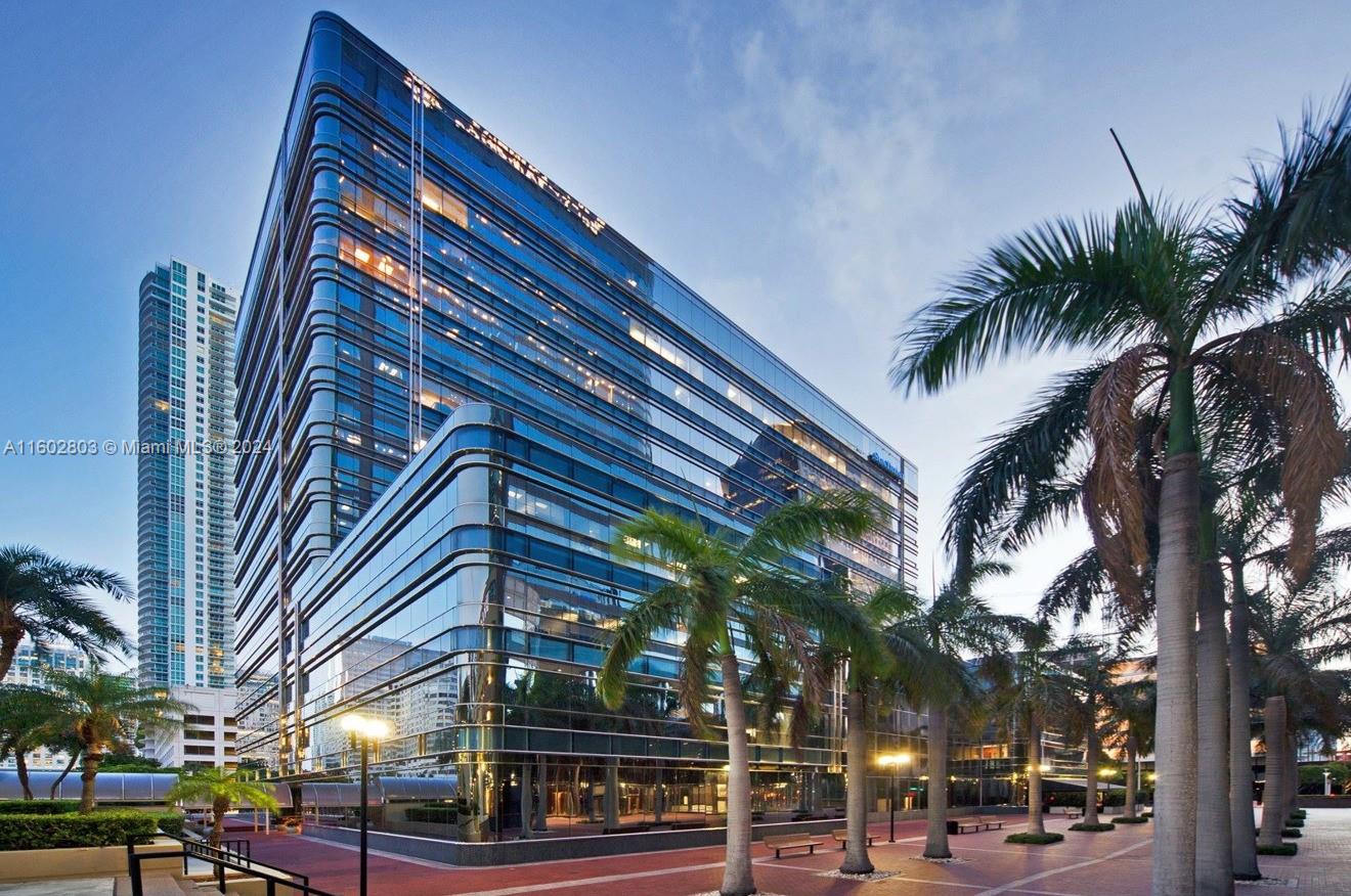 A modern glass office building stands surrounded by palm trees on a paved plaza — 777 Brickell Ave, Miami FL 33131, MIAMI, FL