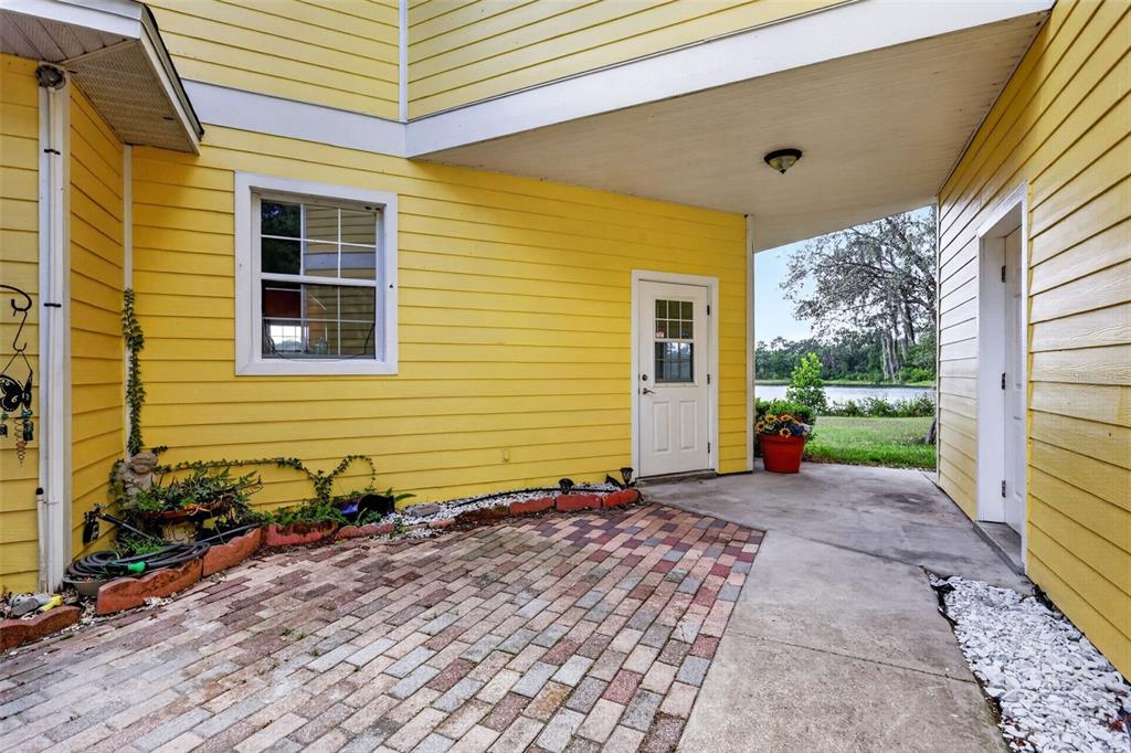 A yellow house exterior features a brick patio, a covered walkway, and a lake view — 493 MALAUKA LOOP, OCKLAWAHA, FL