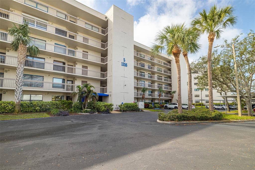 A multi-story apartment building with balconies and palm trees in a paved parking lot — 1316 PASADENA AVENUE S UNIT 204, SOUTH PASADENA, FL