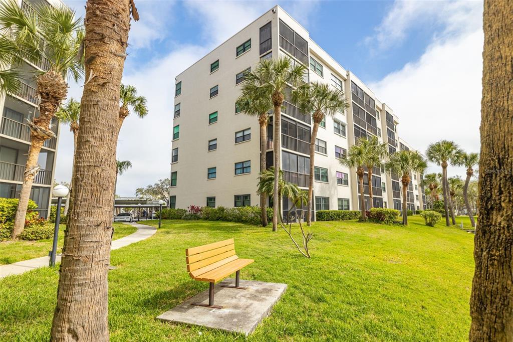 A multi-story apartment building stands behind a grassy lawn with a wooden park bench — 1316 PASADENA AVENUE S UNIT 204, SOUTH PASADENA, FL