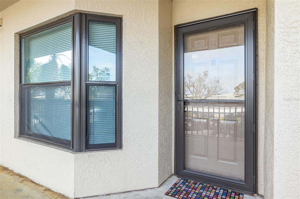 A beige stucco exterior wall features a bay window and a glass storm door — 1316 PASADENA AVENUE S UNIT 204, SOUTH PASADENA, FL