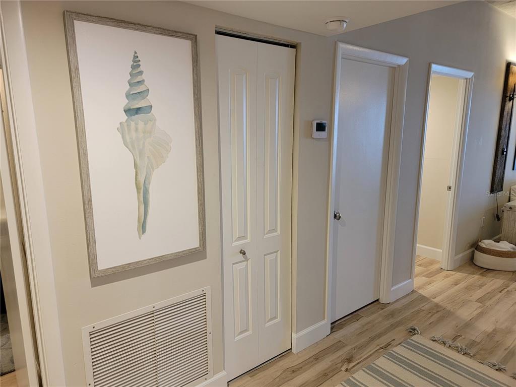 A hallway features light wood-look flooring, a framed seashell print, and several white interior doors — 7650 BAYSHORE DRIVE UNIT 302, TREASURE ISLAND, FL