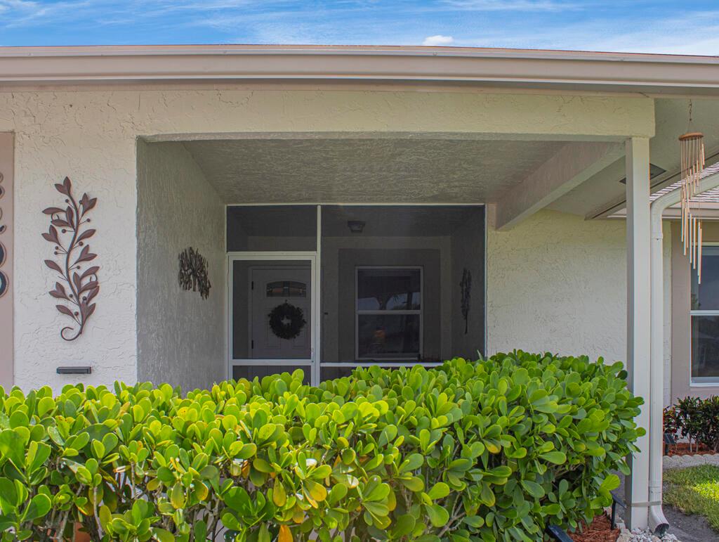 A view of a home's front entrance featuring a screened porch and a green hedge — 3290 Belleville Road # 3290, West Palm Beach FL 33417, WEST PALM BEACH, FL