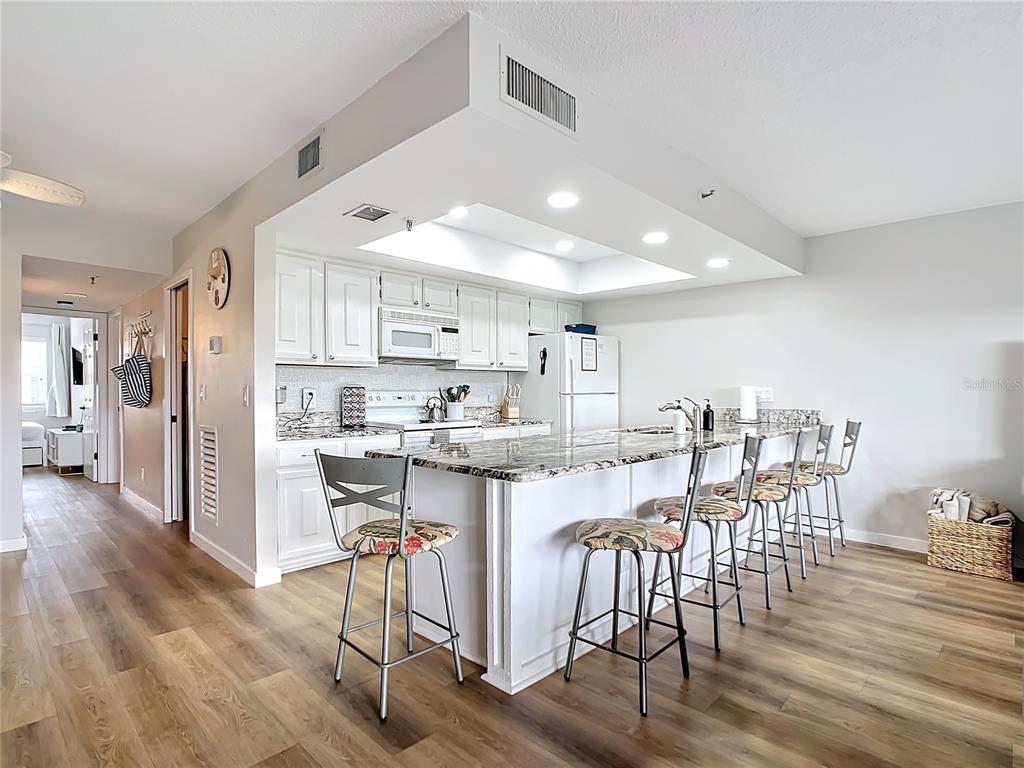 A kitchen features white cabinetry, granite countertops, a breakfast bar with stools, and wood flooring — 19727 GULF BOULEVARD UNIT G1, INDIAN ROCKS BEACH, FL