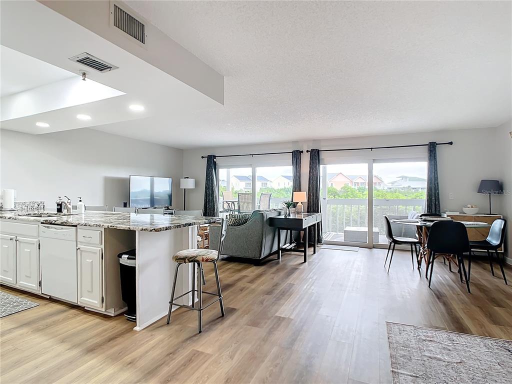 An open-concept living area features a kitchen island, dining space, and sliding glass balcony doors — 19727 GULF BOULEVARD UNIT G1, INDIAN ROCKS BEACH, FL