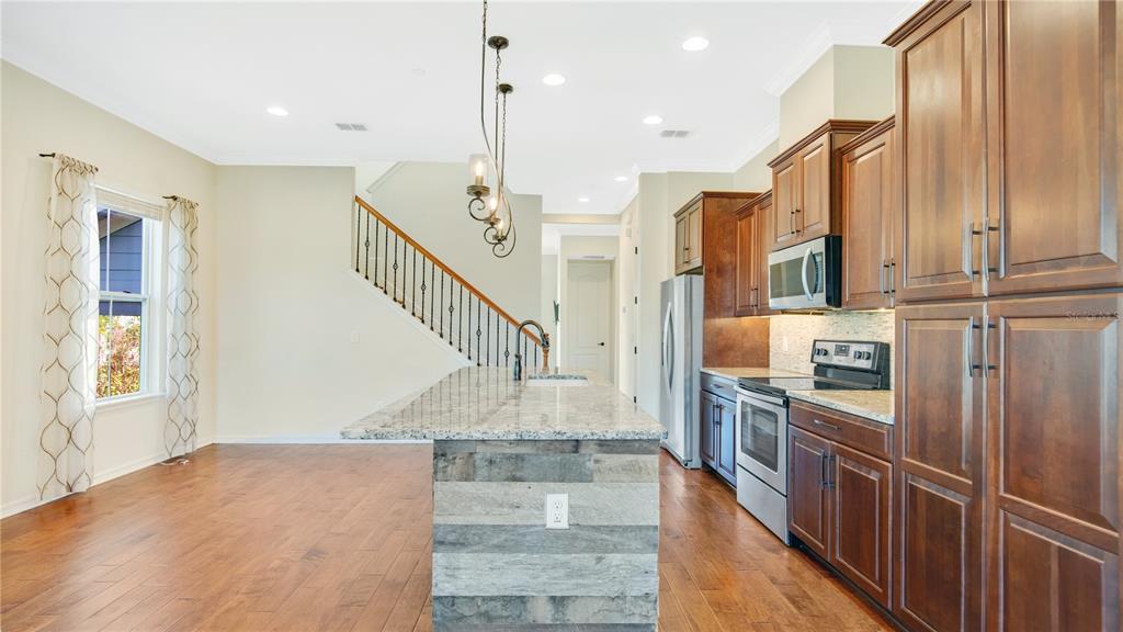 A kitchen with wood cabinets, a granite-topped island, and hardwood floors next to a staircase — 921 TARAMUNDI DRIVE, OVIEDO, FL