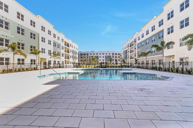 A swimming pool sits between two large, multi-story apartment buildings with a paved patio area — 1220 SOUTHSTATION PLACE UNIT 404, ORLANDO, FL