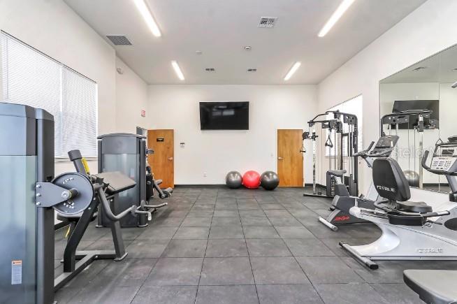 This gym features exercise equipment, rubber flooring, a wall-mounted television, and two wooden doors — 1220 SOUTHSTATION PLACE UNIT 404, ORLANDO, FL
