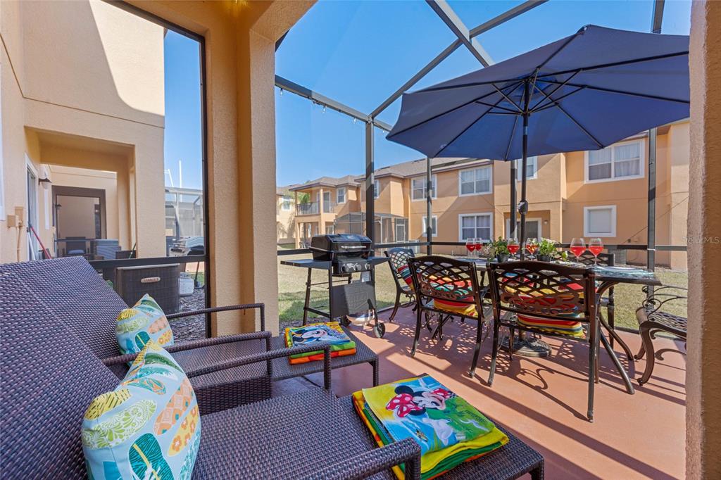 A screened-in patio features outdoor furniture, a grill, and a dining set under an umbrella — 2705 IMPALA LANE, KISSIMMEE, FL
