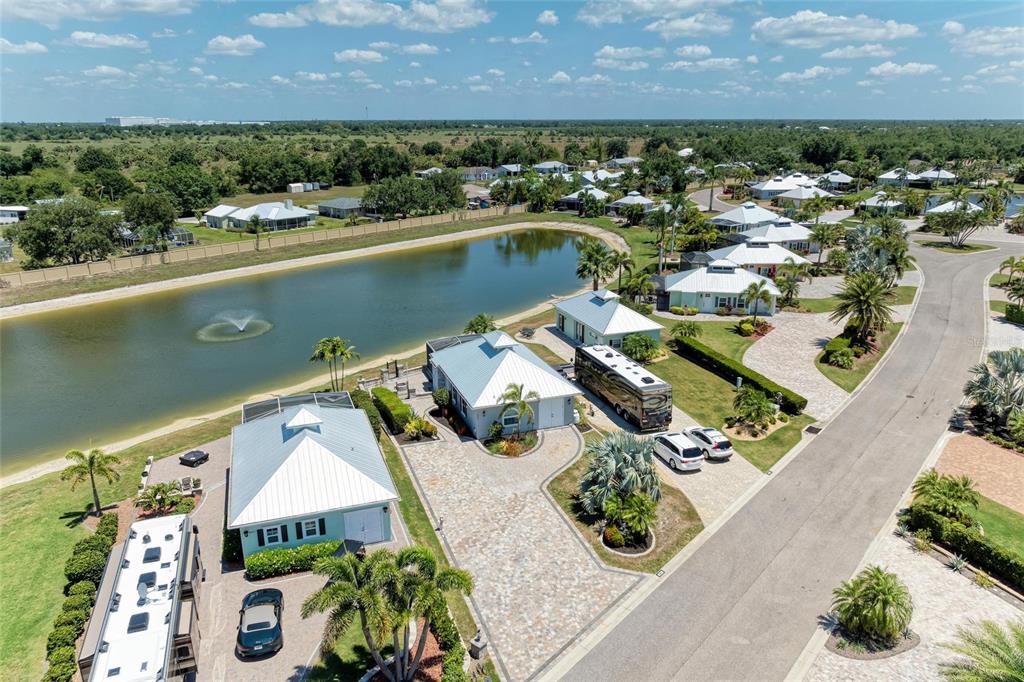 An aerial view shows houses with metal roofs, paved driveways, and RVs beside a pond — 8239 SW SAND CRANE CIRCLE LOT 11, ARCADIA, FL