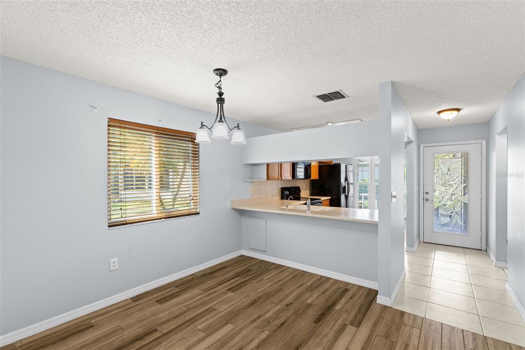 A dining area with wood-look flooring, a window, a chandelier, and a kitchen pass-through — 4534 SLIPPERY ROCK ROAD, NEW PORT RICHEY, FL