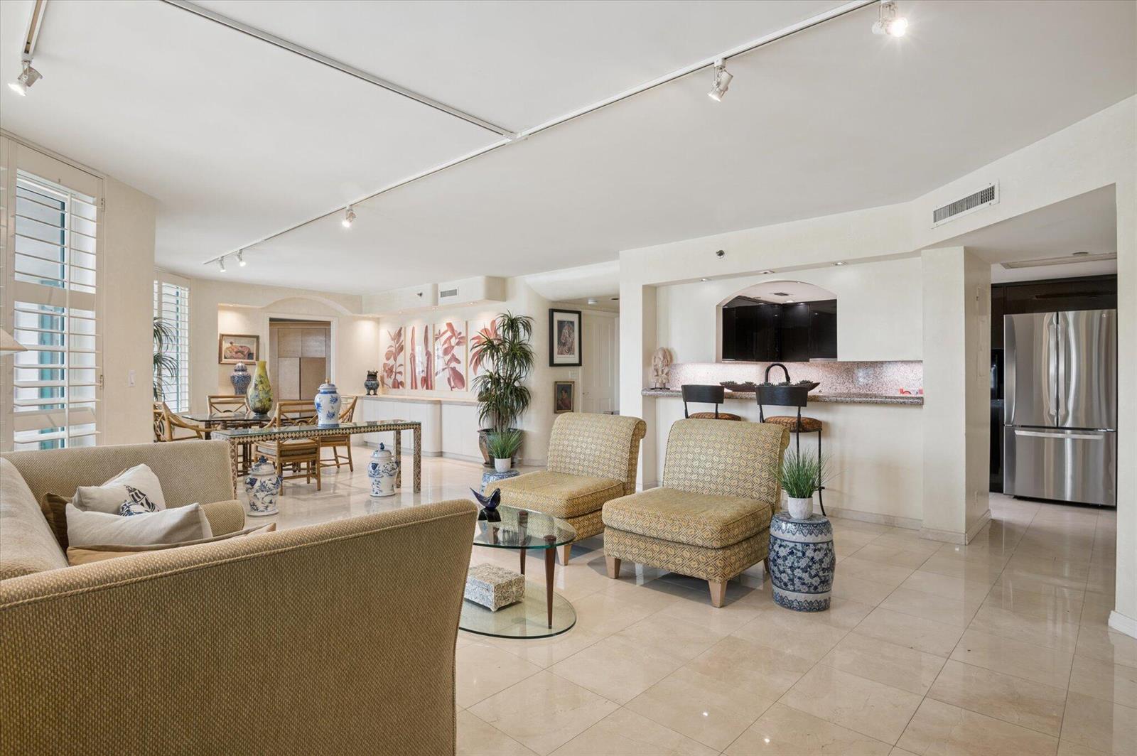 A living room with beige tile floors, patterned armchairs, a glass coffee table, and bar seating — 120 SE 5th Avenue # 329, Boca Raton FL 33432, BOCA RATON, FL